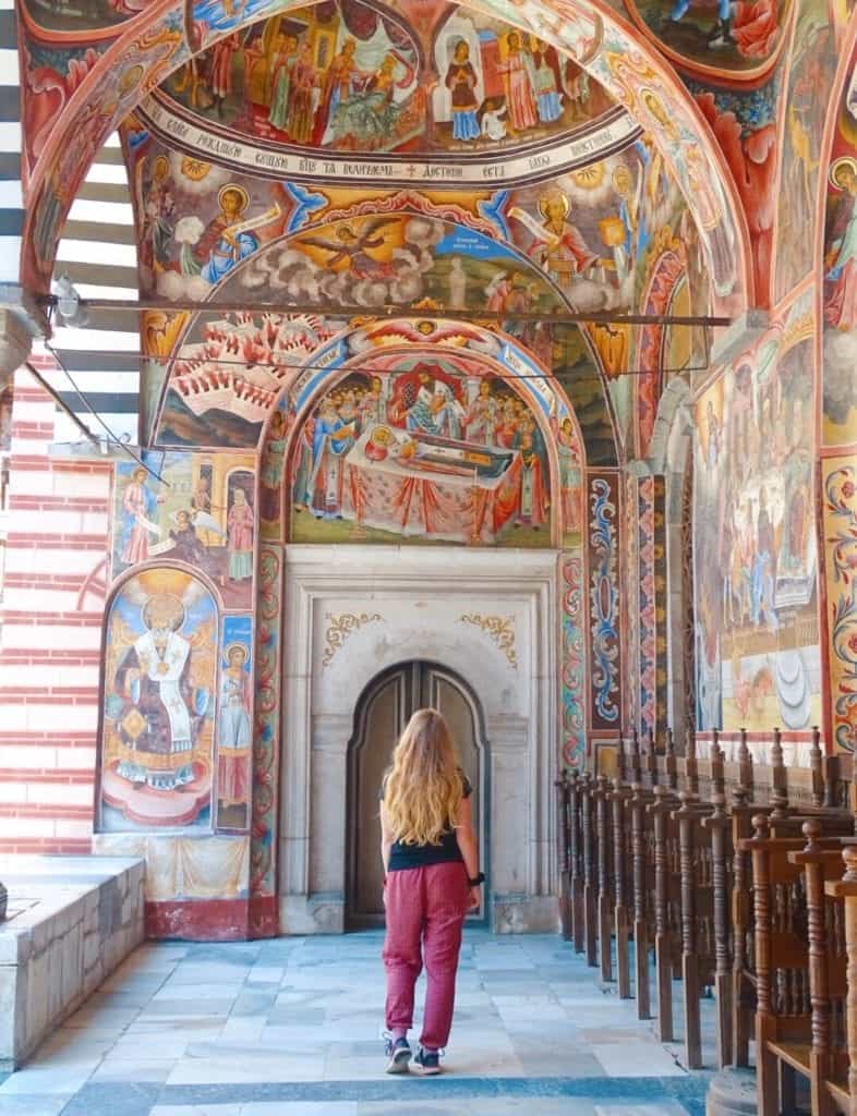 Girl walking through painted hallways at Rila Monastery