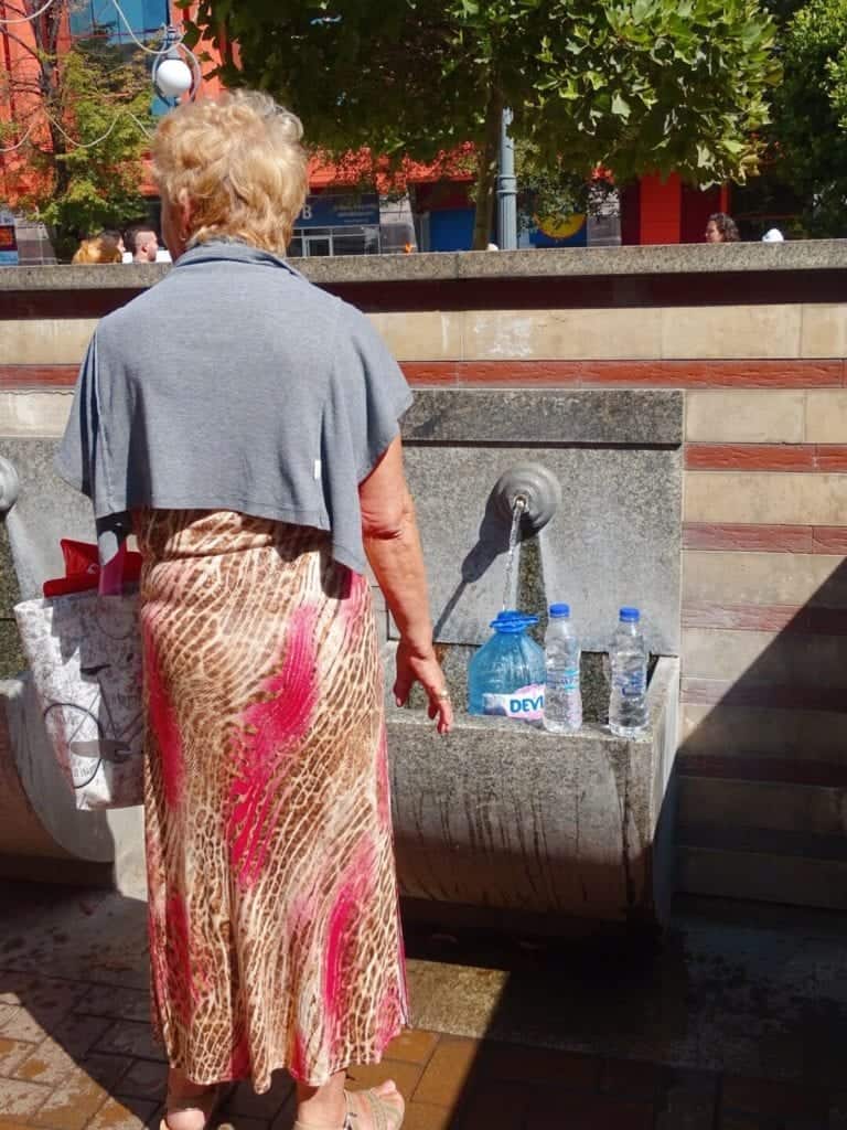 Woman filling up plastic bottles from tap at Central Mineral Baths Sofia Bulgaria 